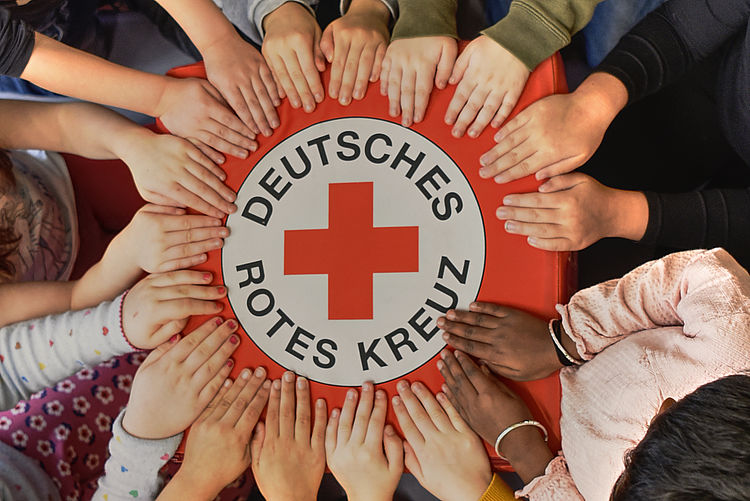 Viele Hände halten das DRK Logo