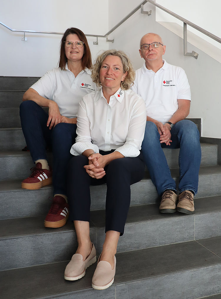 DRK Betreuungsverein Das Team von drei Personen sitzt auf einer Treppe