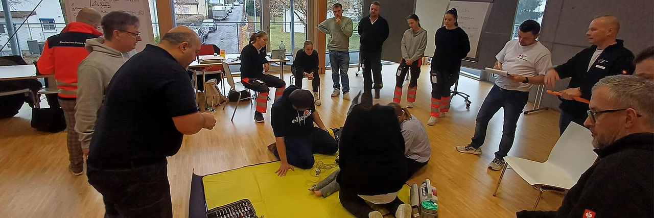 Teilnehmer sitzen bei einer Erste HIlfe Übung auf dem Boden